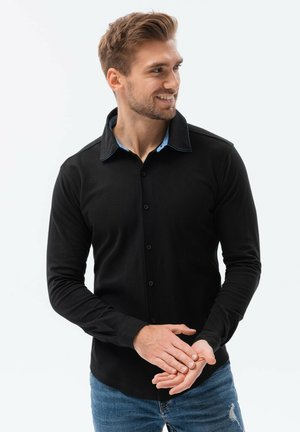 Camisa de manga larga negra con botón y un cuello y puños en un azul claro que contrasta, presenta un corte regular y una tela texturizada.