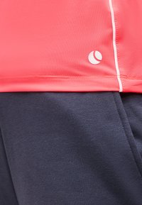 Φωτεινό ροζ αθλητικό τοπ με λευκές λεπτομέρειες πάνω από σκούρο ναυτικό παντελόνι φόρμας, που δείχνει την υφή του υφάσματος και τις λεπτομέρειες των ραφών.