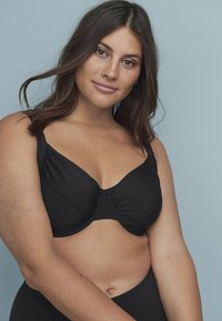 Zwarte beugelbeha met een gladde stofafwerking, voorzien van een V-vormige halslijn, brede bandjes en een naadloos ontwerp.