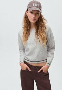 Ljust grått kort sweatshirts med ribbat avslut, matchat med mörkbruna byxor med framfickor. Kapseln har texten "NO DRAMAS" tryckt i vitt.