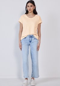Stribet kortærmet t-shirt i lys orange og hvid, parret med lyseblå lige ben jeans og hvide sneakers. Enkel, afslappet outfit.