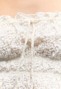 Fehér, texturált szövet közeli képe, amely összehúzott, fodros mintázatú, középen megkötött húzózsinórral.