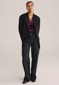 Černý blazer s ostrými klopami, spárovaný s tmavě burgundským saténovým topem s krajkovým lemem a širokými černými jeansy. Hladké textury, propracovaný střih.