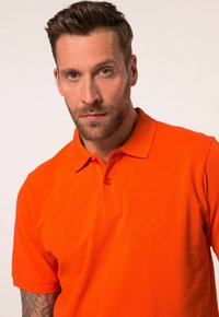Oranges Poloshirt aus Baumwolle. Mit einem Kragen und einer zwei-Knopfleiste. Glatte Textur mit kurzen Ärmeln. Keine sichtbaren Muster oder Akzente.