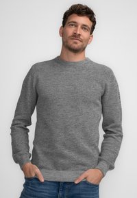Grauer Strickpullover mit Rundhalsausschnitt und langen Ärmeln, der ein strukturiertes Muster aufweist. Klassischer Schnitt, kombiniert mit blauen Jeans.