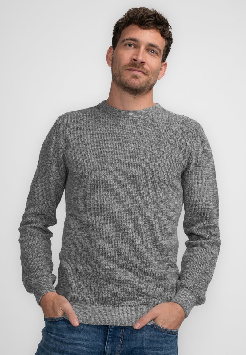 Grauer Strickpullover mit Rundhalsausschnitt und langen Ärmeln, der ein strukturiertes Muster aufweist. Klassischer Schnitt, kombiniert mit blauen Jeans.
