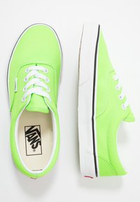 Neongrüne Segeltuch-Sneaker mit weißen Schnürsenkeln und schwarzen Akzenten. Verfügt über ein niedrig geschnittenes Design und eine strukturierte Oberfläche. Markenlogo innen sichtbar.