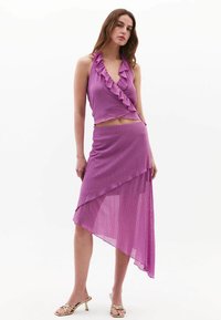 Completo due pezzi viola con top halter arricciato e gonna asimmetrica con una texture trasparente. Sandali dorati con lacci completano il look.