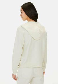 Lichtcrème gebreide hoodie, relaxed fit, met een grote capuchon, ribgebreide mouwen en zoom. De achterkant toont een gelijkmatige textuur en zijsplitten.
