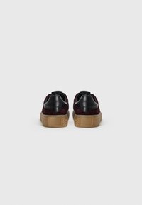 Baskets en daim bordeaux avec des accents en cuir noir, semelle en liège texturée, bout rond et détail du logo sur le talon.
