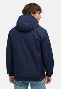 Mørkeblå jakke med hette, med en glatt tekstur, elastiske ermer og ribbestrikket kant. Baksiden har et minimalistisk design uten mønstre.