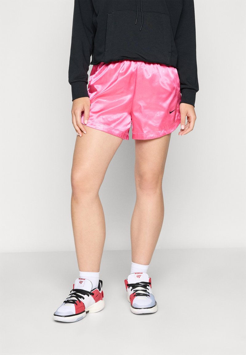 Rosa satengidrettsbukser med glatt tekstur og snor i livet, parret med svart hettegenser og flerfargede sneakers.