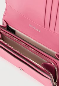 Ροζ δερμάτινο πορτοφόλι με πολλαπλές θήκες, ασημένιες λεπτομέρειες φερμουάρ και ανάγλυφο λογότυπο. Το εσωτερικό διαθέτει λείο ύφασμα και θήκες για κάρτες.