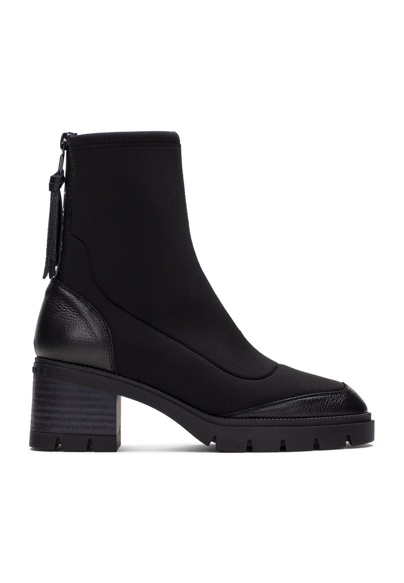Botas negras hasta el tobillo con un tacón de cuero texturizado, parte superior de tejido suave y suela de goma estriada. Cuenta con un zipper lateral y un detalle de borlas.