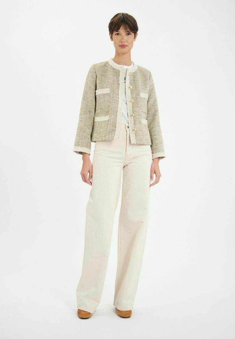Veste en tweed beige avec des accents blancs, présentant un col rond, des manches courtes et de grands boutons. Assortie à un pantalon large crème.