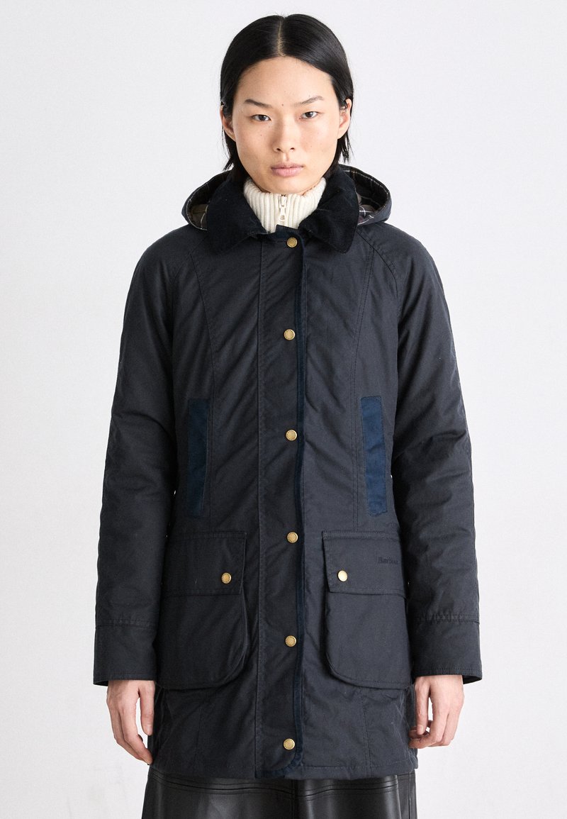 Marineblauwe lange jas met gouden knopen, een corduroy kraag, twee voorzakken, verticale blauwe zijpanelen en een patroonvoering binnenin de capuchon.