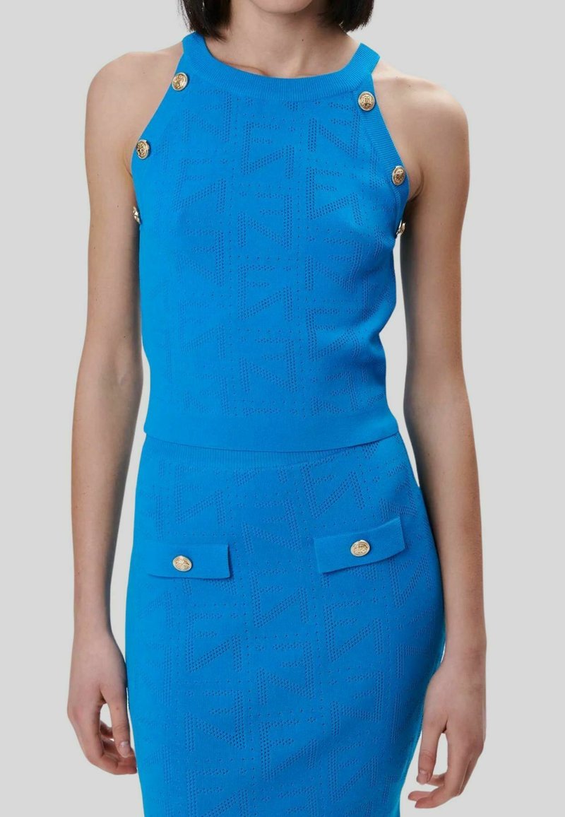 Maglia blu lavorata a maglia con bottoni dorati sulle spalle e una gonna aderente abbinata con tasche decorative e motivi testurizzati.