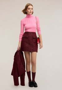 Rosa ribbad polotröja, vinröd texturerad minikjol med fickor, kombinerad med knälånga vinröda strumpor och svarta loafers.