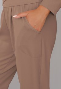 Brązowe dresy z elastycznym pasem i bocznymi kieszeniami. Gładka tekstura, luźny krój, widoczne detale w szwie.