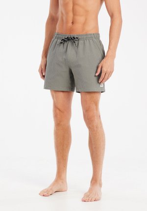 Shorts de bain pour hommes en vert olive avec une surface texturée. Dotés d'une taille élastique avec cordon de serrage et de poches latérales.