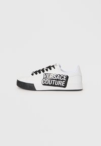 White leather sneaker with black accents and laces. Features a large black logo label on the side, textured sole with embossed branding.