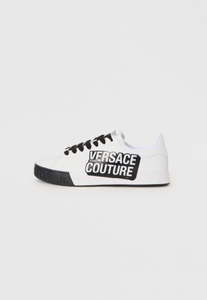 Baskets blanches en cuir avec accents et lacets noirs. Présente une grande étiquette logo noire sur le côté, semelle texturée avec marquage en relief.