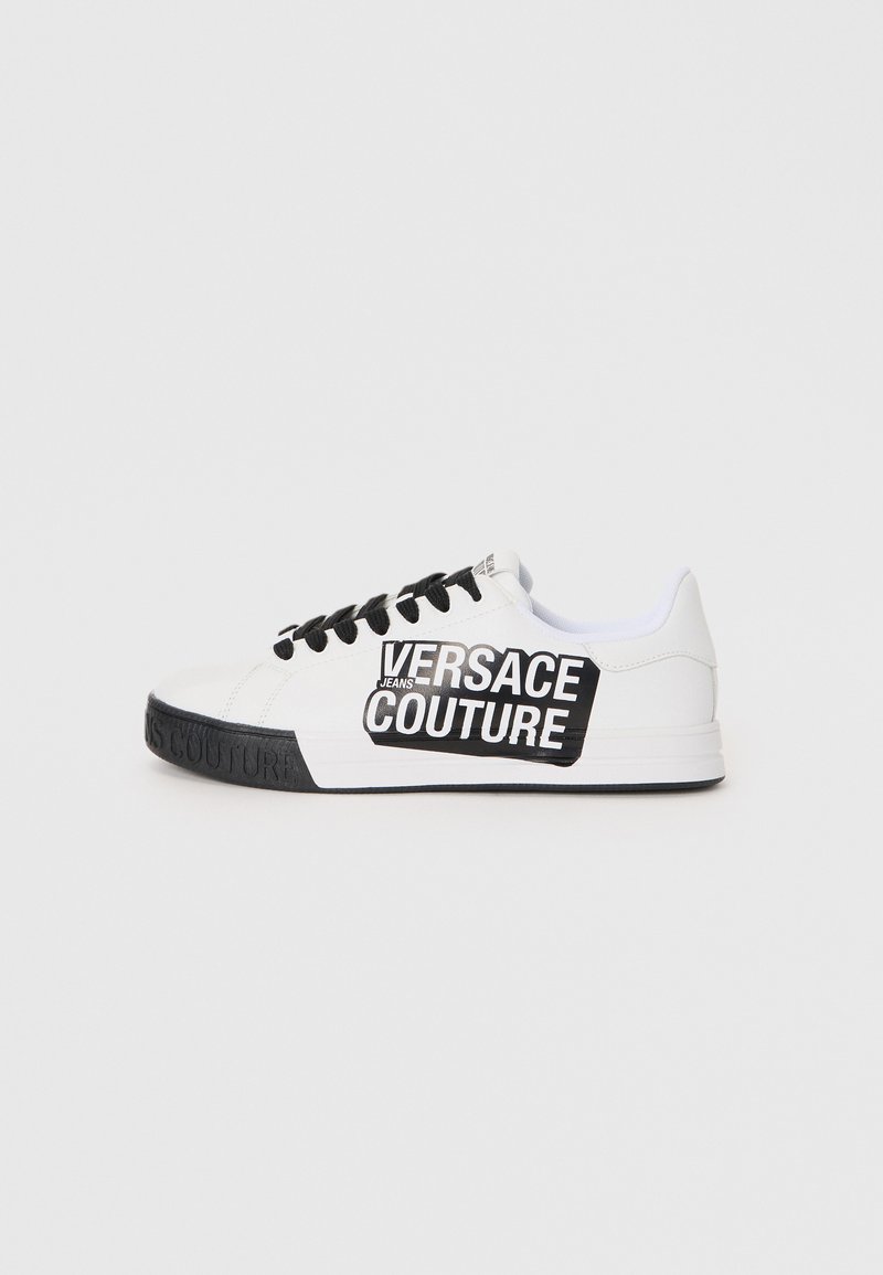 White leather sneaker with black accents and laces. Features a large black logo label on the side, textured sole with embossed branding.