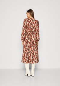 Abito lungo beige con una vivace stampa animale rossa, viola e marrone. Presenta maniche lunghe e una vita cin cin, abbinato a stivali bianchi al ginocchio.