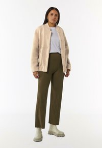 Beżowa polarowa kurtka z przednimi kieszeniami, szary t-shirt, oliwkowe prążkowane spodnie i kremowe botki za kostkę z grubymi podeszwami. Prosty, teksturowany strój.