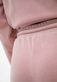 Różowy zestaw odzieży dresowej z weluru o miękkiej teksturze. Pasek w talii jest elastyczny, a szwy starannie przeszyte, co nadaje schludny wygląd.