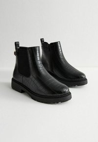 Botas Chelsea negras con textura de piel de cocodrilo, paneles laterales elásticos, suela duradera y una correa decorativa en el tobillo.