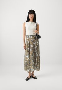 Top alb cu bretele, fustă lungă cu model floral în nuanțe de aur, albastru și alb, asortată cu pantofi negri fără toc și o geantă mică neagră.
