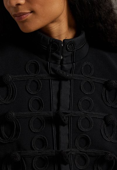 Μαύρο ύφασμα μπουφάν με ψηλό γιακά και διακοσμητικές λεπτομέρειες από πλεγμένο σκοινί κατά μήκος του μπροστινού μέρους, με υφή.