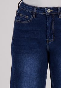 Donkerblauwe denim jeans met een soepele textuur. Kenmerken zijn onder meer een knoopsluiting, een voorzak en contrastgeel stiksels.