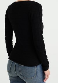 Haut noir à manches longues avec un motif texturé, coupe ajustée et encolure ronde, assorti à un jean bleu taille mi-haute.