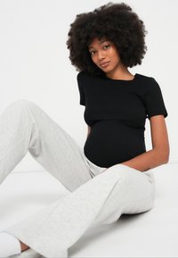 Black ribbed short-sleeve top paired with light gray soft wide-leg pants. The model is seated with a visible pregnant belly.