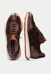 Braune Sneaker mit Leopardenmuster-Textur, glatten Lederakzenten und einer kontrastierenden hellen Sohle. Schnürsenkel und Branding sind sichtbar.