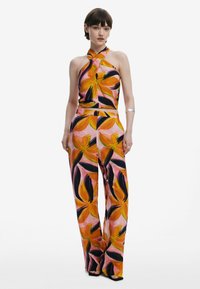 Completo due pezzi con stampa floreale, composto da un top con collo all'americana e schiena scoperta, abbinato a pantaloni a gamba larga in arancione, rosa e nero su uno sfondo chiaro.