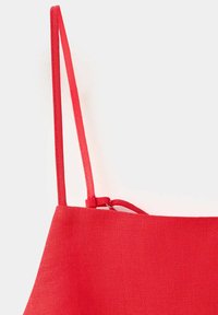 Sac cabas en tissu rouge vu depuis le coin supérieur avec de fines bretelles rouges sur fond blanc.