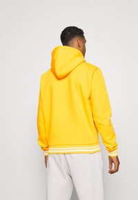 Sudadera amarilla con una gran capucha, puños acanalados y un dobladillo a rayas. El material parece suave, con una textura lisa y un ajuste relajado.