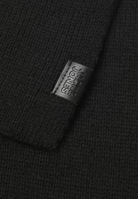 Black knitted scarf with a soft texture, featuring a rectangular shape and a leather label with embossed text on one side.