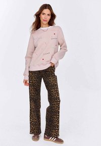 Světle růžová mikina s vícebarevným textem a grafikou srdce, spárovaná s hnědými kalhotami s leopardím potiskem a hnědými teniskami s bílými pruhy.