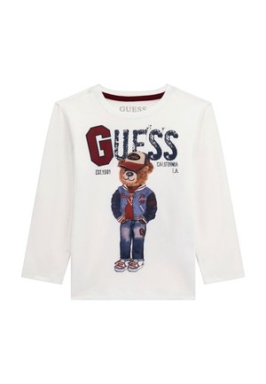 Hvid langærmet skjorte med en bjørn iført varsityjakke, jeans, sneakers og kasket med teksten "GUESS" og "California L.A.".