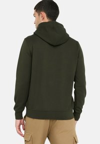 Donkergroen sweatvest met capuchon in een zachte, gestructureerde stof. Voorzien van een kangeroezak en geribbelde manchetten, ontworpen met een recht model.