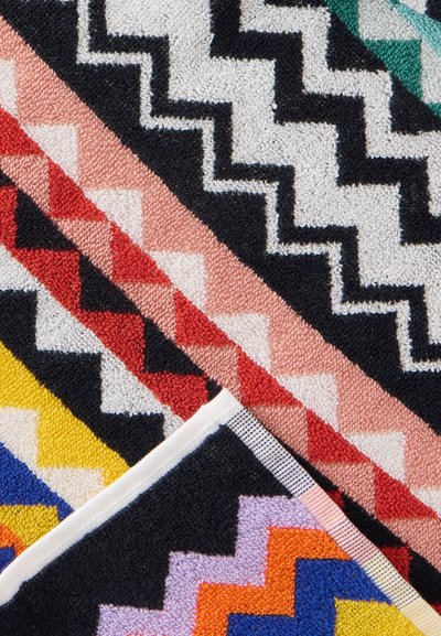 Serviettes colorées avec des motifs géométriques en zigzag et triangulaires en noir, blanc, rouge, rose, jaune, bleu et orange disposées en chevauchement.