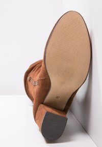 Botte en suède marron avec un talon épais, présentant une semelle striée, des accents cousus et une surface supérieure lisse. Taille indiquée comme 37.