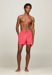 Bañador corto rosa con cintura elástica y cordón ajustable. Fabricado en tejido ligero, de longitud por encima de la rodilla, con bolsillos laterales. Adecuado para el uso en verano.
