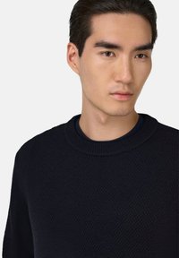 Marineblauwe gebreide trui met een gestructureerd oppervlak, ronde halslijn en geribbelde mouwen. Eenvoudig, veelzijdig ontwerp geschikt voor casual draag.