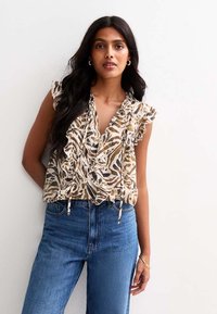Floral-patterned blouse in beige and brown with ruffled short sleeves, paired with high-waisted blue denim jeans. Textured fabric detail visible.