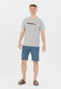 Grå kortärmad t-shirt med "YELLOWSTONE" grafik. Matcher med blå uppvikt shorts och bruna sandaler med rem och spänne.